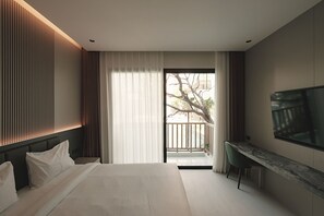A modern hotel room with a bed, a desk, a TV, and a balcony with a view of trees. - AFTER RAIN HOTEL (Chiang Mai)