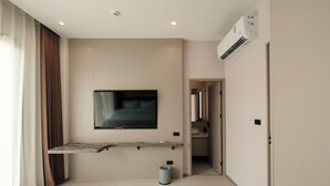 A modern hotel room with a mounted TV, a small trash bin, and a hallway leading to a bathroom. - AFTER RAIN HOTEL (Chiang Mai)
