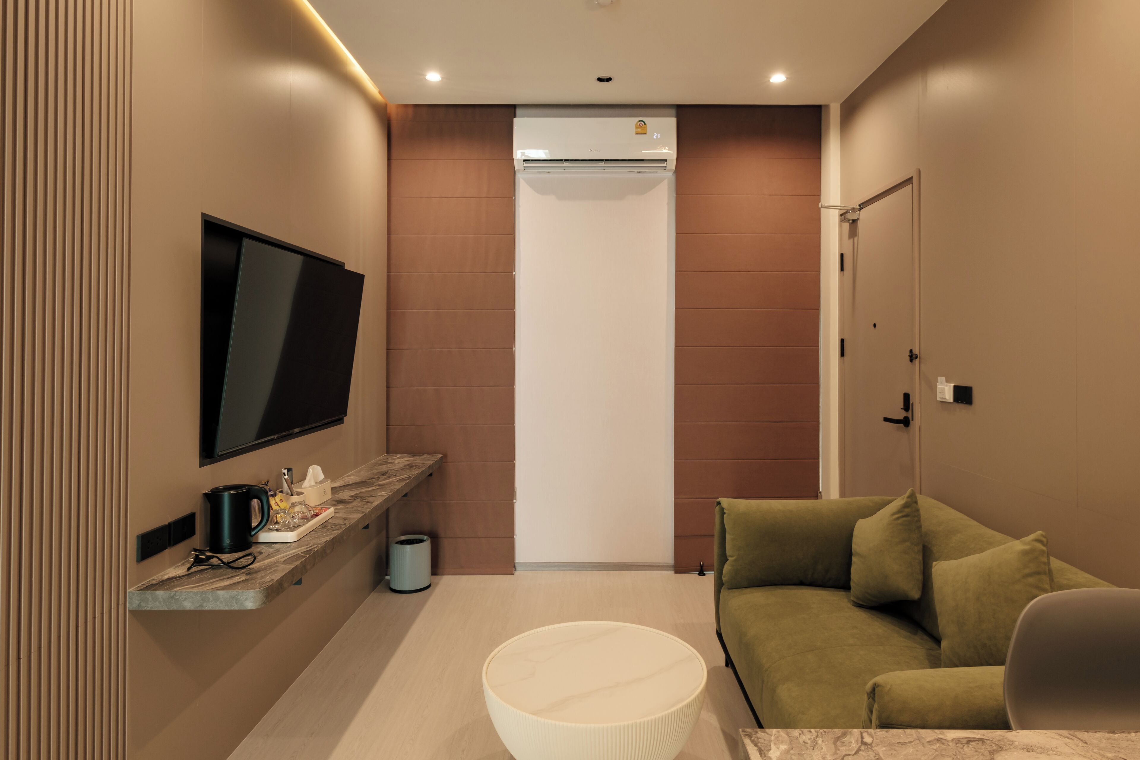 A modern bathroom with a built-in air conditioning unit, a mounted television, a vanity with a sink, and a green sofa.