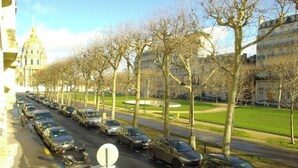 A street lined with parked cars and leafless trees, leading to a large building with a dome. - Wake up beside Napoleon (Paris)