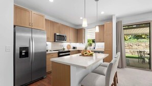 A modern kitchen with wooden cabinets, stainless steel appliances, and a central island with bar stools. - @ Marbella Lane | Hale Laʻi Serene Luxury 3BR Home (Waianae)