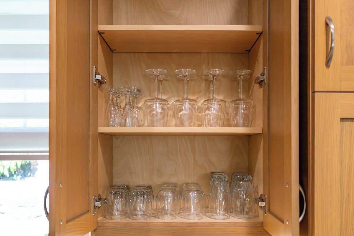 Un mueble de madera con dos estantes, cada uno con cristalería y frascos transparentes.
