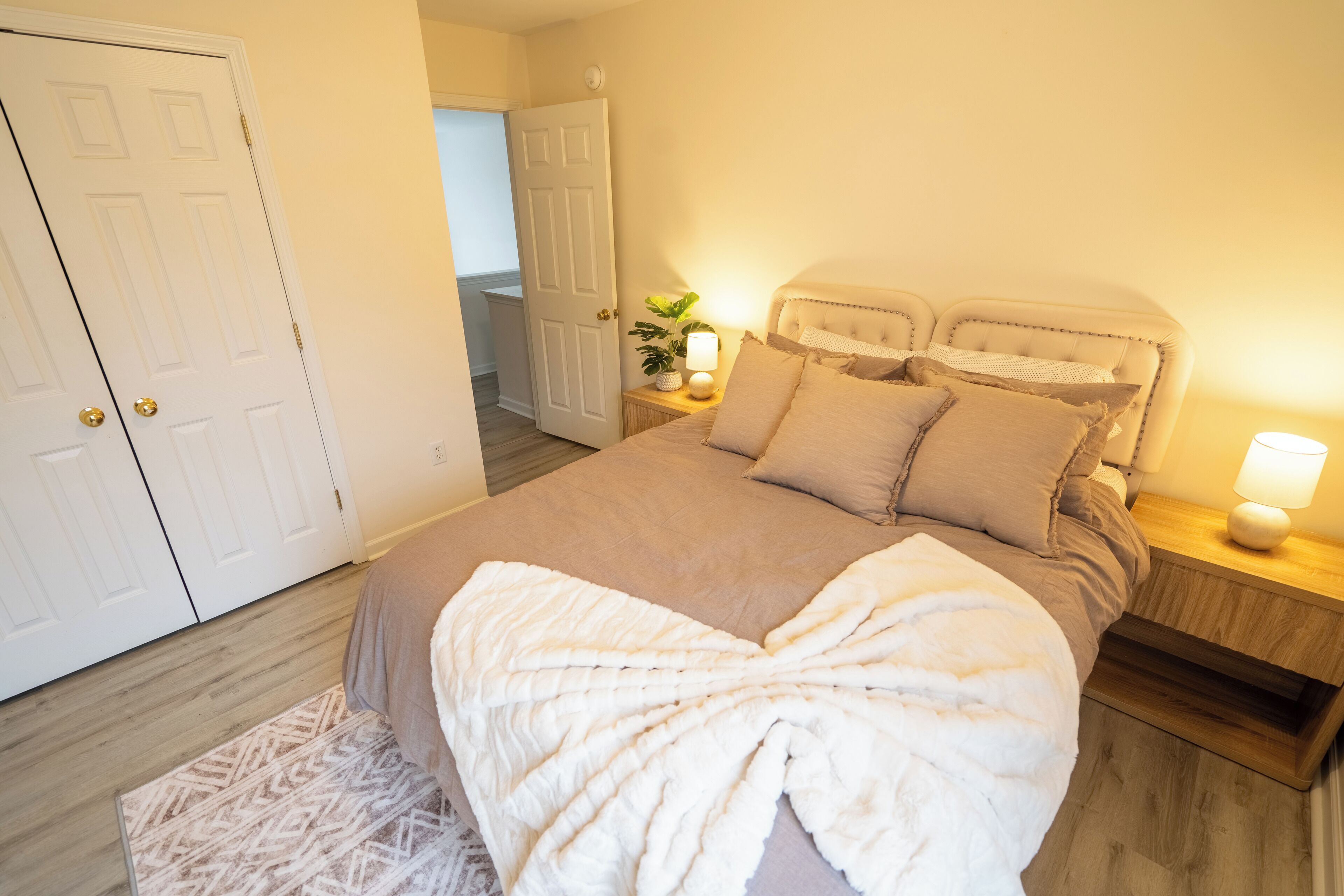 A bedroom with a bed, bedside tables, a nightstand, a lamp, and a door.