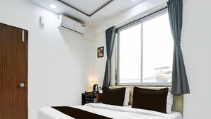 Una habitación de hotel con cama, escritorio, aire acondicionado y ventana con cortinas.