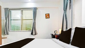 Habitación de hotel con una cama grande, un escritorio con lámpara y una ventana con cortinas.