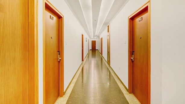 A long, narrow hallway with wooden doors on both sides, leading to individual rooms. - Townhouse City Center Kushal Nagar (Somvarpet)
