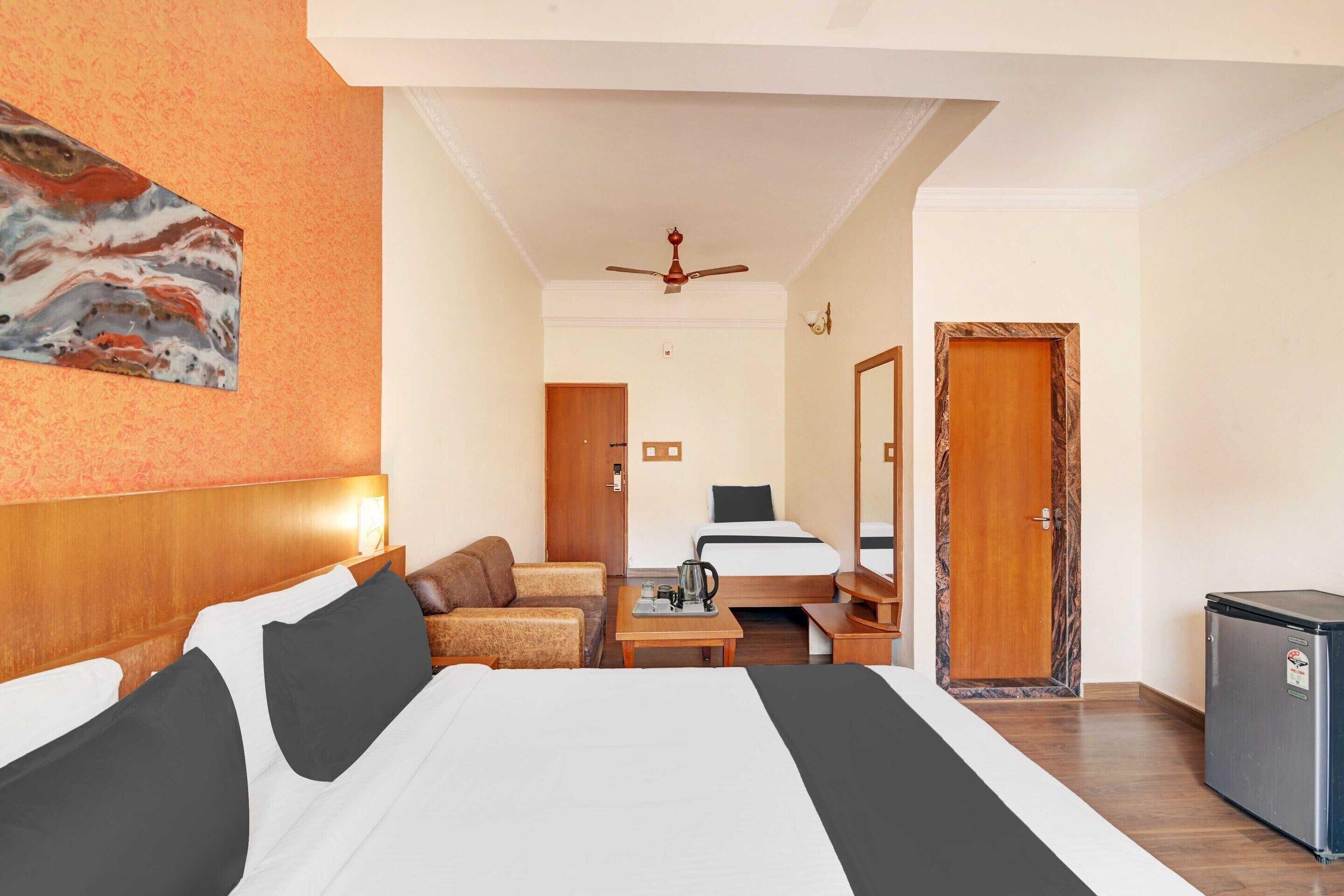 A hotel room with a large bed, a desk, a chair, a small refrigerator, and a ceiling fan.