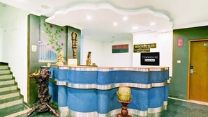 A reception desk with a blue and white design, a sign indicating it's a reception area, and a staircase to the left. - Townhouse City Center Kushal Nagar (Somvarpet)
