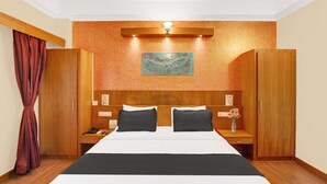 A hotel room with a large bed, wooden headboard, a nightstand, a desk, a mirror, a wardrobe, and a painting on the wall. - Townhouse City Center Kushal Nagar (Somvarpet)