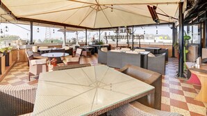 An outdoor seating area with wicker furniture, a glass table, and a large umbrella providing shade. - Townhouse City Center Kushal Nagar (Somvarpet)