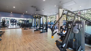 Une salle de sport équipée de divers appareils d’exercice, dotée d’un plancher en bois et de grandes fenêtres laissant entrer la lumière naturelle.