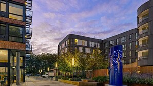 Un bâtiment moderne doté d’une cour intérieure, d’une sculpture bleue et d’un fourgon garé devant.
