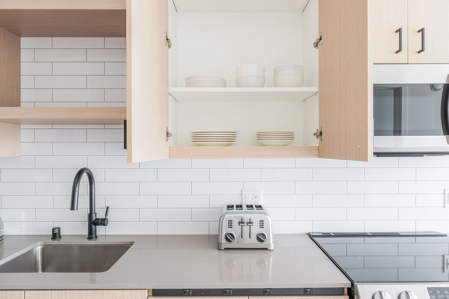 Een moderne keuken met een witte betegelde achterwand, een roestvrijstalen spoelbak, een broodrooster en een magnetron.