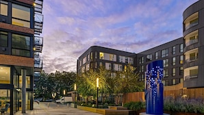 Un bâtiment moderne doté d’une cour intérieure, d’une sculpture bleue et d’un fourgon garé devant.