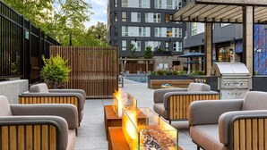 Un espace extérieur aménagé avec des meubles modernes, une table en verre avec un foyer intégré, et une piscine en arrière-plan.