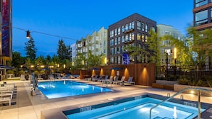Un espace piscine comprenant deux piscines, des chaises longues et un bâtiment à plusieurs étages avec des balcons en arrière-plan.