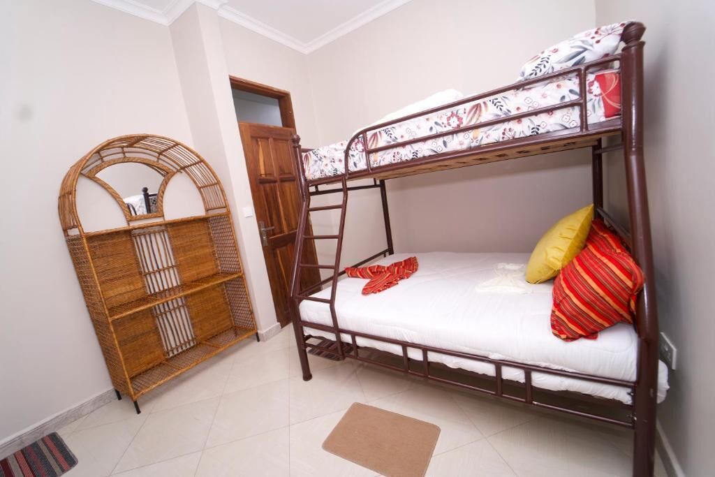 Una cama litera con escalera, un estante de ratán y una puerta que da a otra habitación.