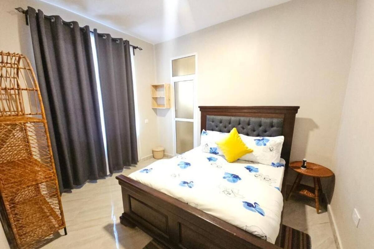 A bedroom with a bed, a bedside table, a lamp, a window with curtains, and a chair.