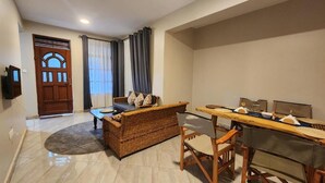 A compact living space with a sofa, a dining table, and a television. - Pembeni River House (Arusha)