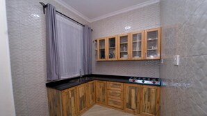 A compact kitchen with wooden cabinets, a gas stove, and a grey tiled backsplash. - Pembeni River House (Arusha)