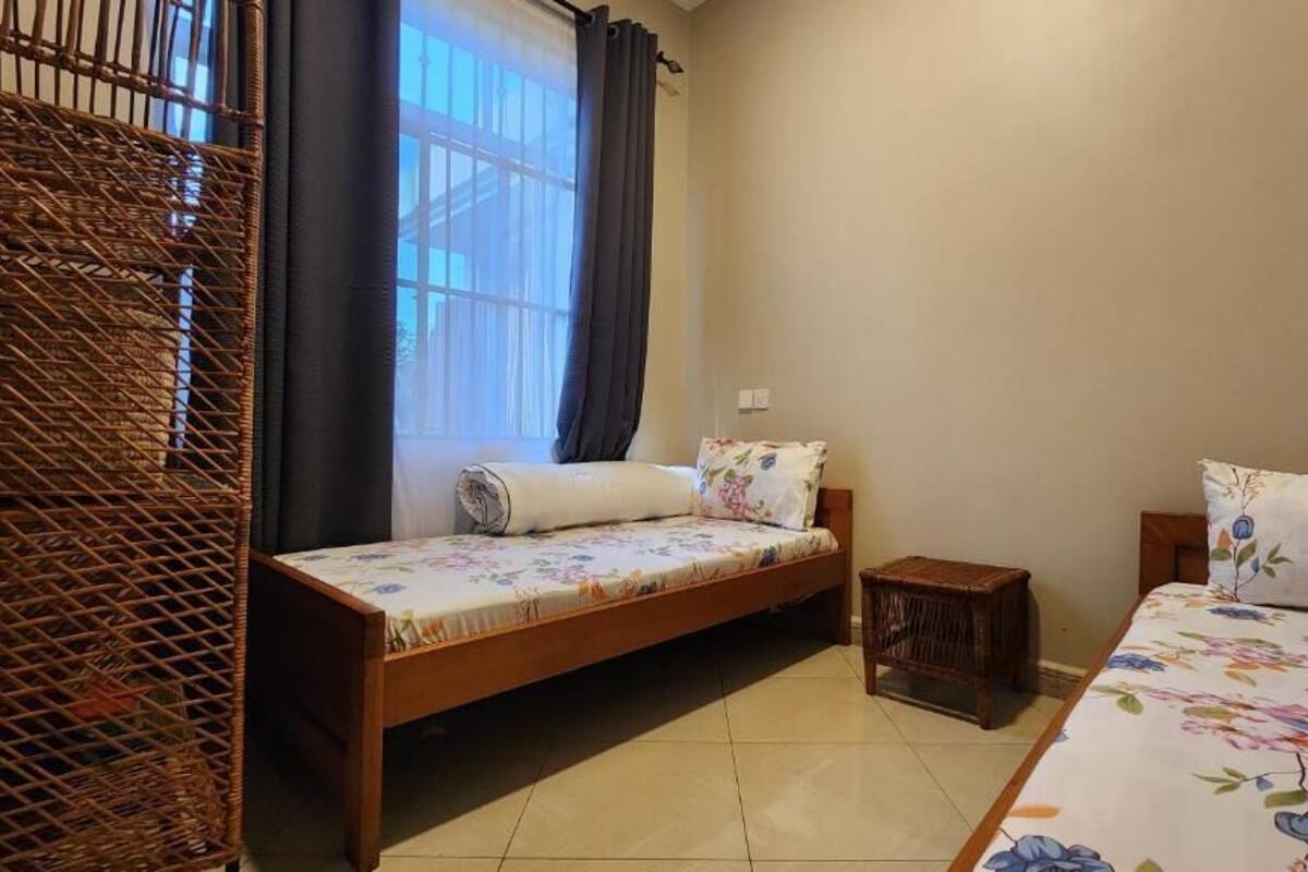 A room with a bed, a small table, a wicker chair, and a window with curtains.