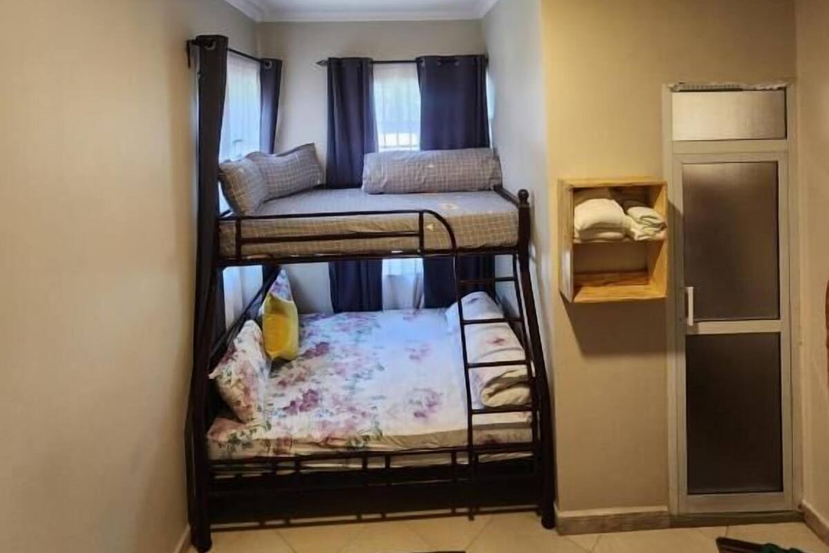 A compact room with a bunk bed, a small wooden shelf, and a door.