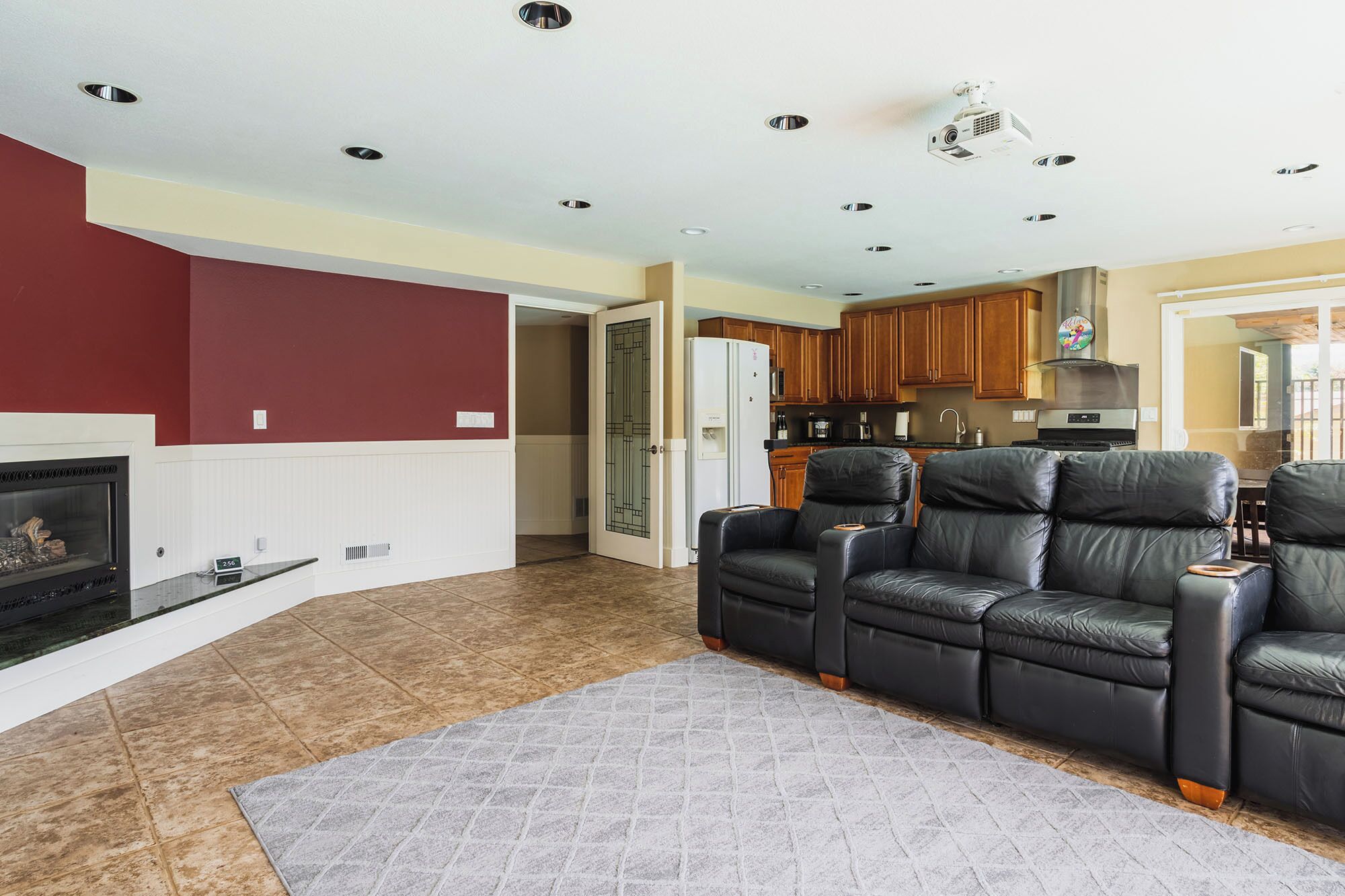 A living room with a fireplace, a large black leather sofa, and a kitchen in the background.