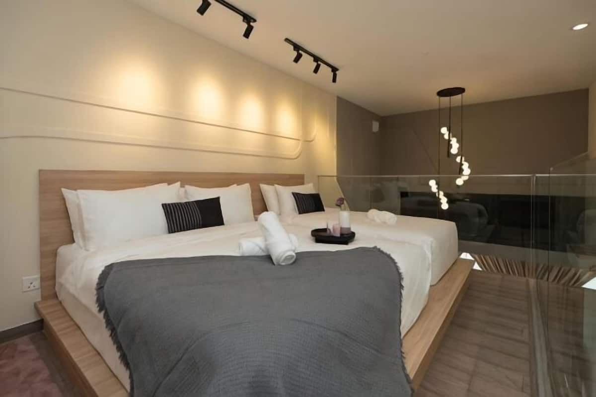 Habitació d'hotel moderna amb un llit gran, taules de nit, un separador de vidre i vista a la ciutat.