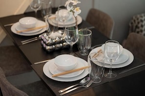 Une table à manger dressée avec de l’assiette blanche, des bols, des baguettes et des verres.