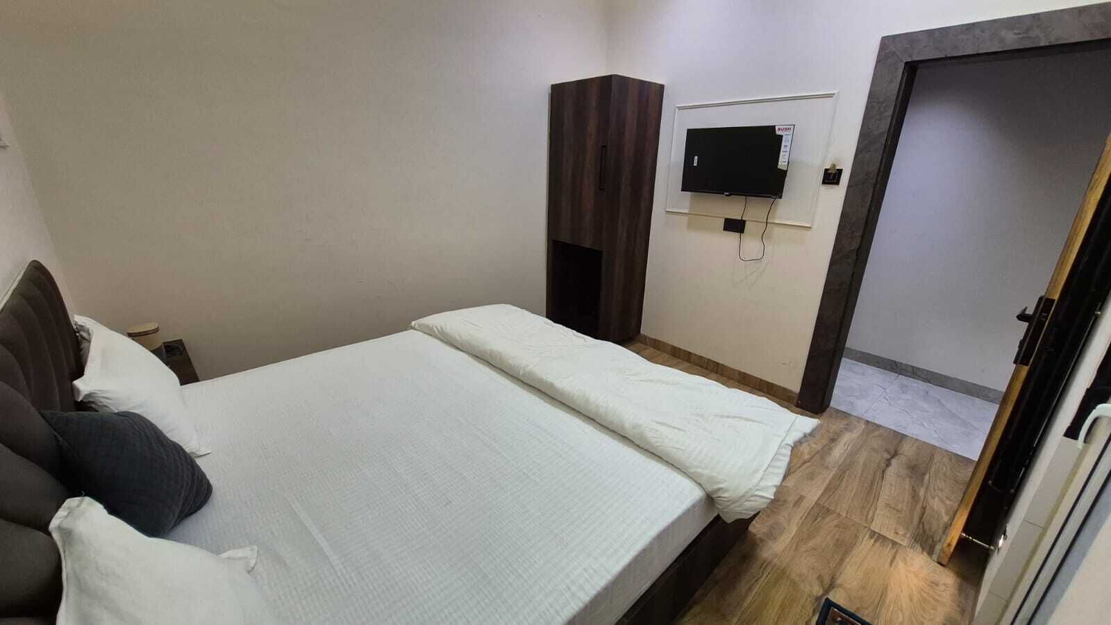 Ένα υπνοδωμάτιο με ένα κρεβάτι, μια τηλεόραση τοποθετημένη στον τοίχο και μια πόρτα που οδηγεί σε ένα άλλο δωμάτιο.