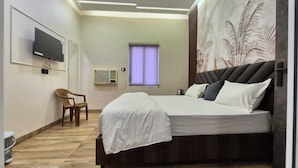 Una camera d'hotel moderna con un letto, una TV a muro, una finestra con tende e una sedia.