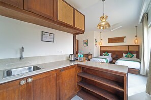Una cucina con lavello, pensili in legno e un piano di lavoro. Si vede un letto con testiera in legno e due cuscini.