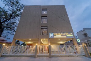 Un edificio moderno con un cartello dell'hotel 'Treebo', caratterizzato da una facciata semplice con tre finestre e un ingresso con cancello.