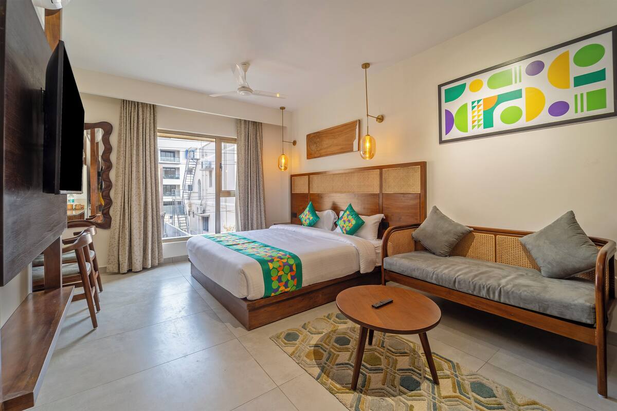A hotel room with a bed, sofa, TV, and a balcony with curtains.