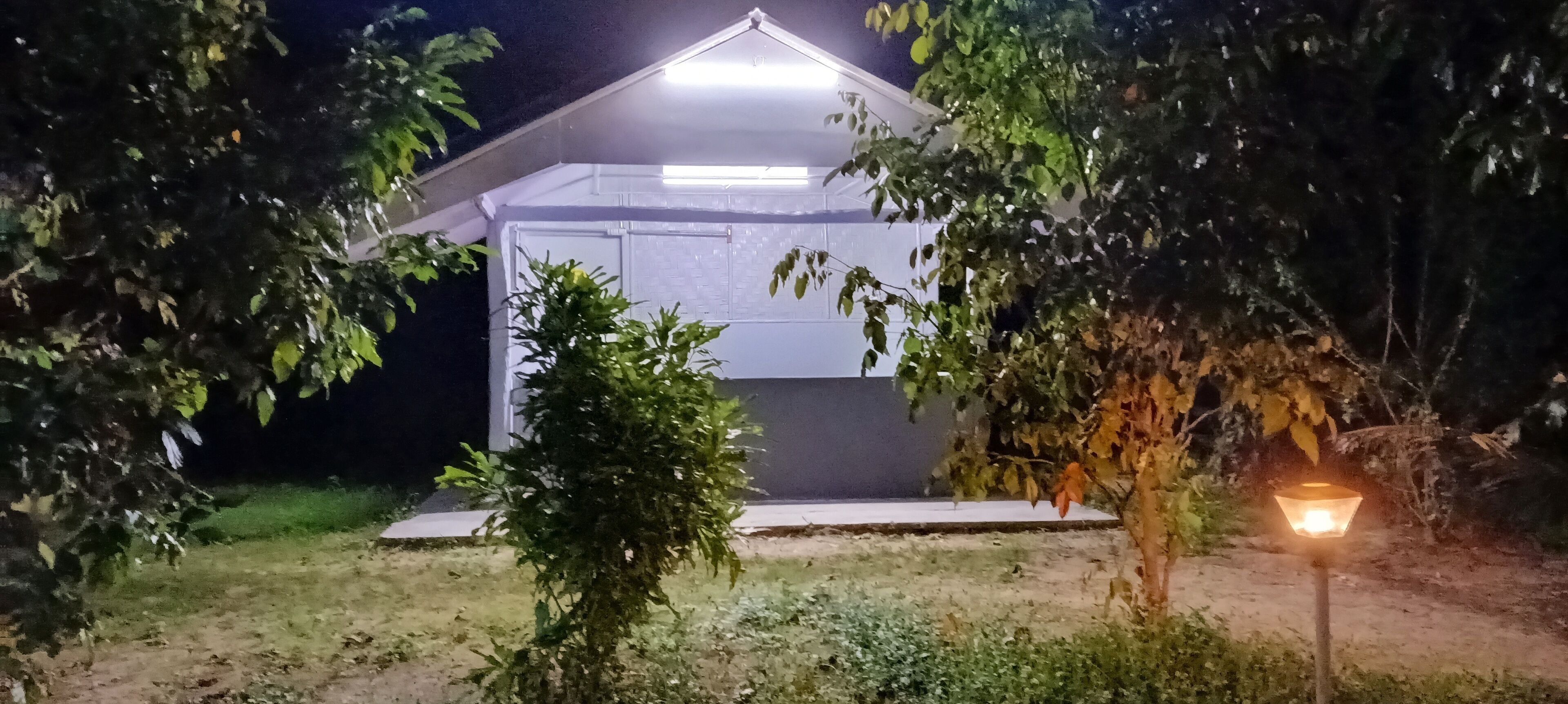 Un edificio con techo plano y un pequeño porche, rodeado de árboles y césped.