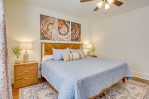 Une chambre à coucher avec un grand lit, une tête de lit en bois, deux tables de chevet avec des lampes et un ventilateur de plafond.