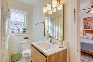 Une salle de bain avec des toilettes, un lavabo et un miroir. Il y a une fenêtre avec des rideaux et une plante sur le rebord de la fenêtre.