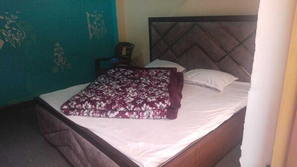 A bed with a floral blanket, a wooden headboard, and a nightstand with a lamp. - Rishi River View (Rajgarhi)