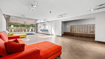 A spacious lobby with a red sofa, a yellow sofa, and a blue bench. There is a wall of mailboxes and a reception desk.