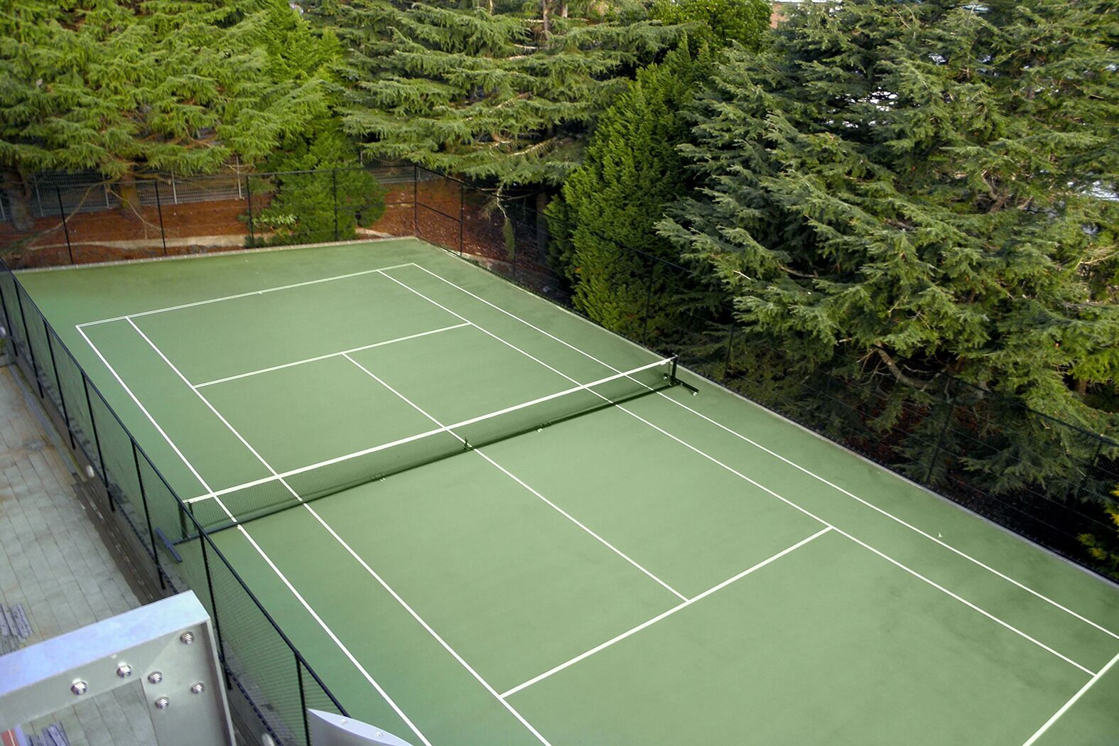 Tenniskenttä, jossa on verkko, ja jonka ympärillä on tiheää puustoa.