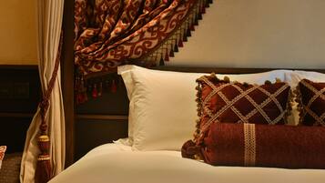 Una cama con sábanas blancas, almohadas rojas, cortina estampada y cabecero de madera.
