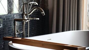 A modern bathroom with a freestanding bathtub, a visible showerhead, and a window with a view of the outside.