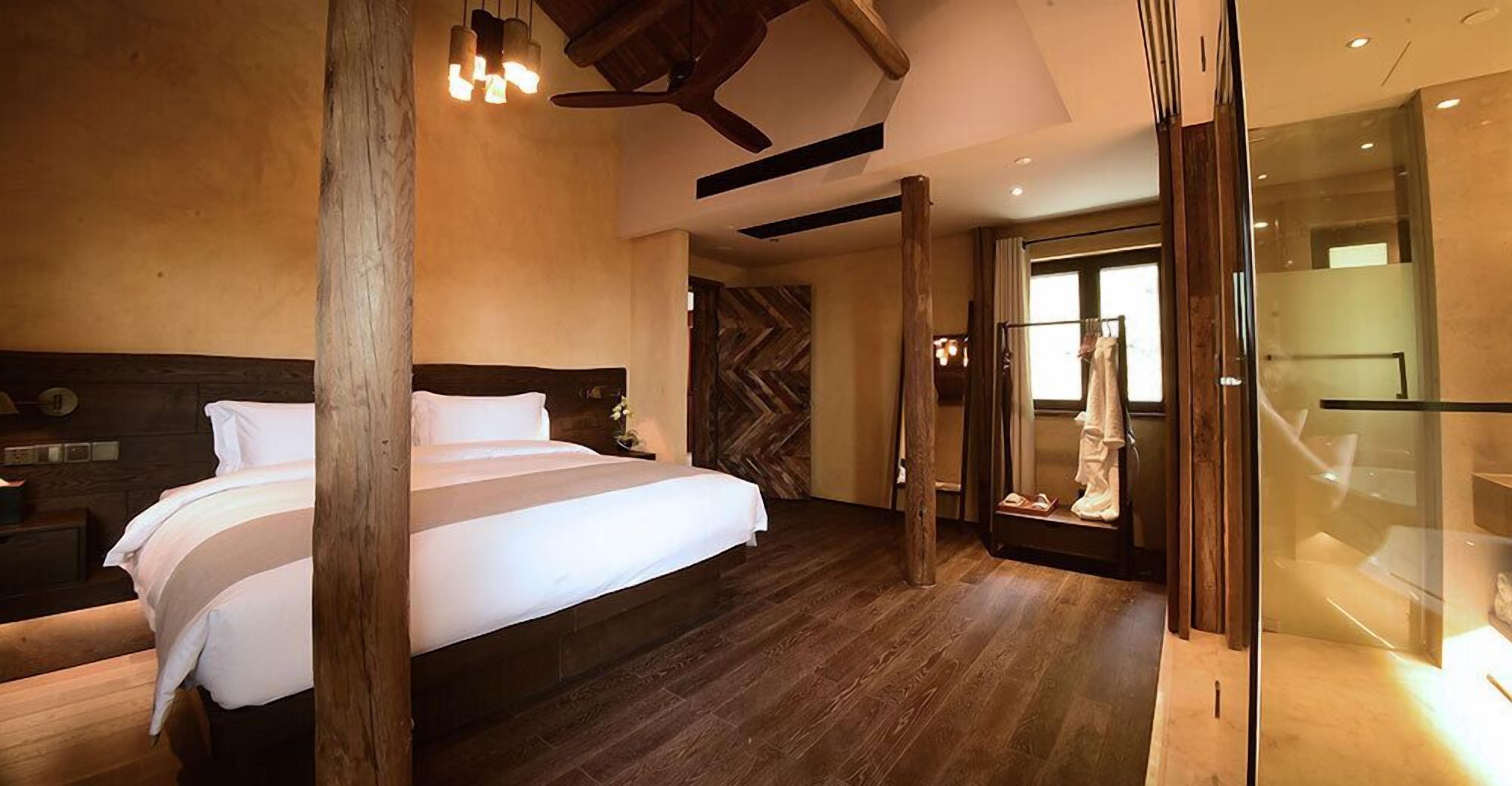 Un dormitorio moderno con una cama grande, vigas de madera, un ventilador de techo y una cabina de ducha de vidrio.