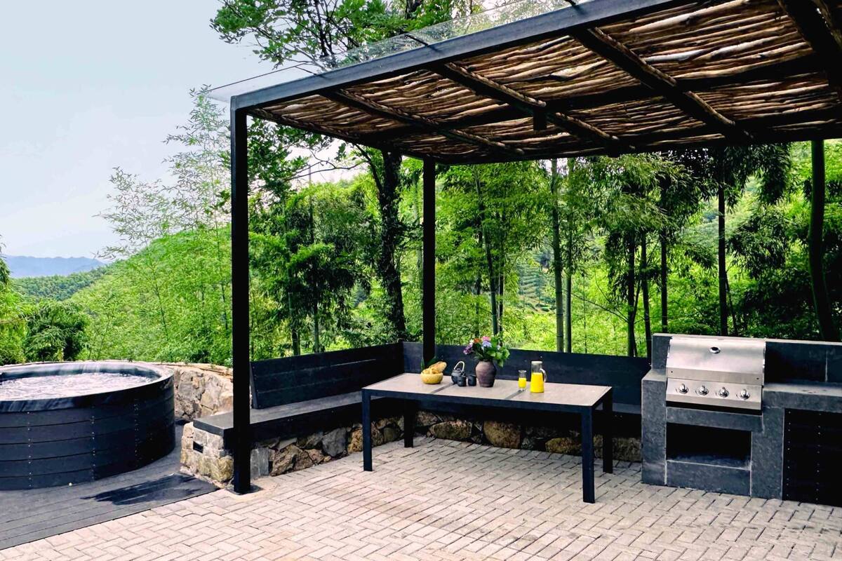 Un patio exterior con un jacuzzi de piedra, una parrilla y una mesa con bebidas y un florero.