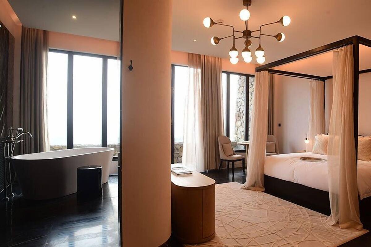 Un dormitorio moderno con cama con dosel, un ventanal grande y un baño separado con bañera.