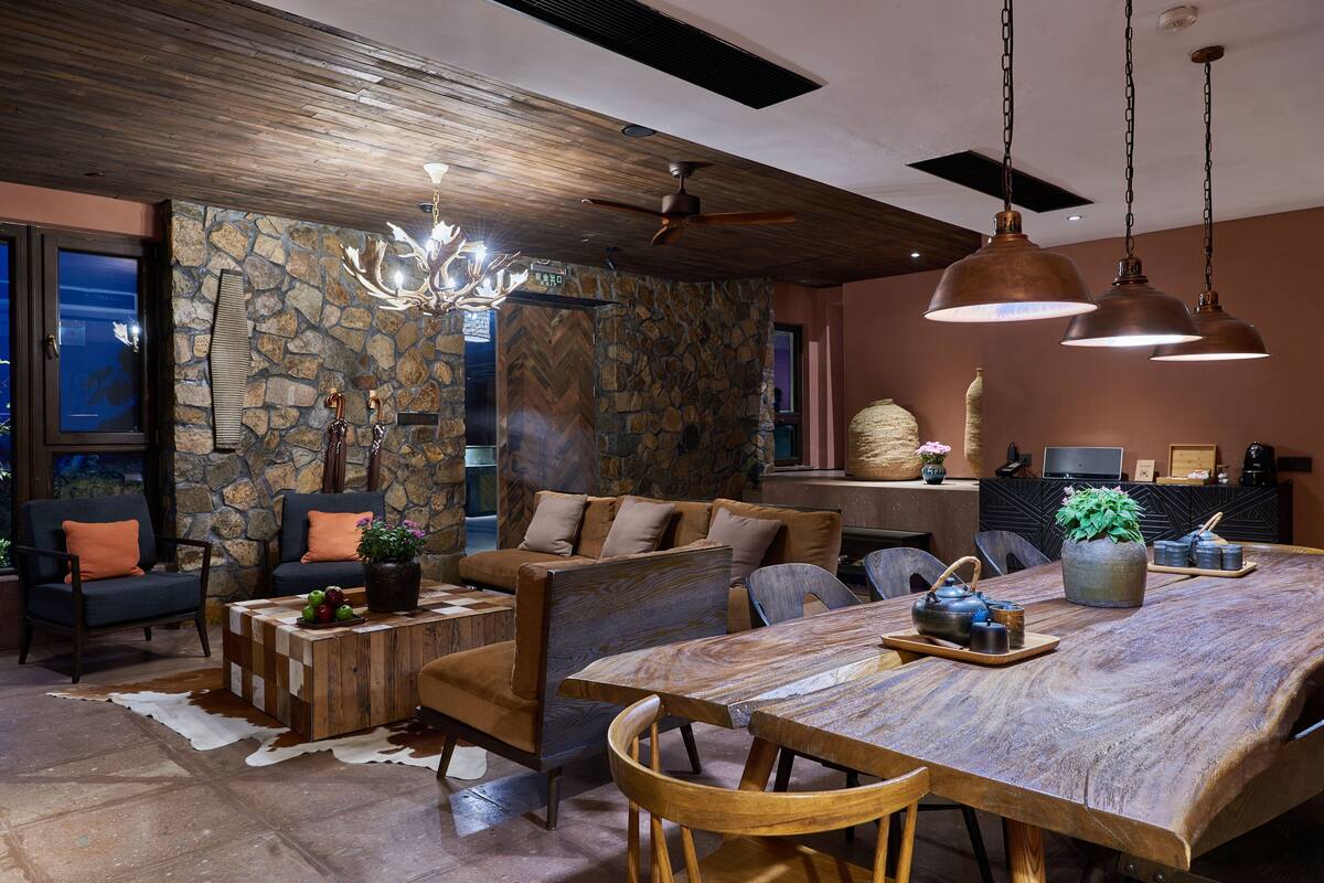 Un amplio salón con una gran mesa de madera, asientos cómodos, una pared decorativa de piedra y un ventilador de techo.