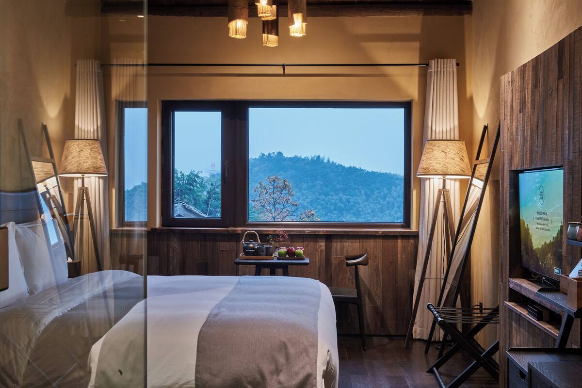 Una habitación de hotel con una cama grande, un escritorio con lámpara, una silla y un televisor.