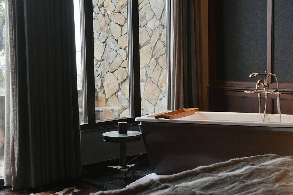 Un baño con pared de piedra, una bañera, una mesita redonda pequeña con una taza y una alfombra de piel.
