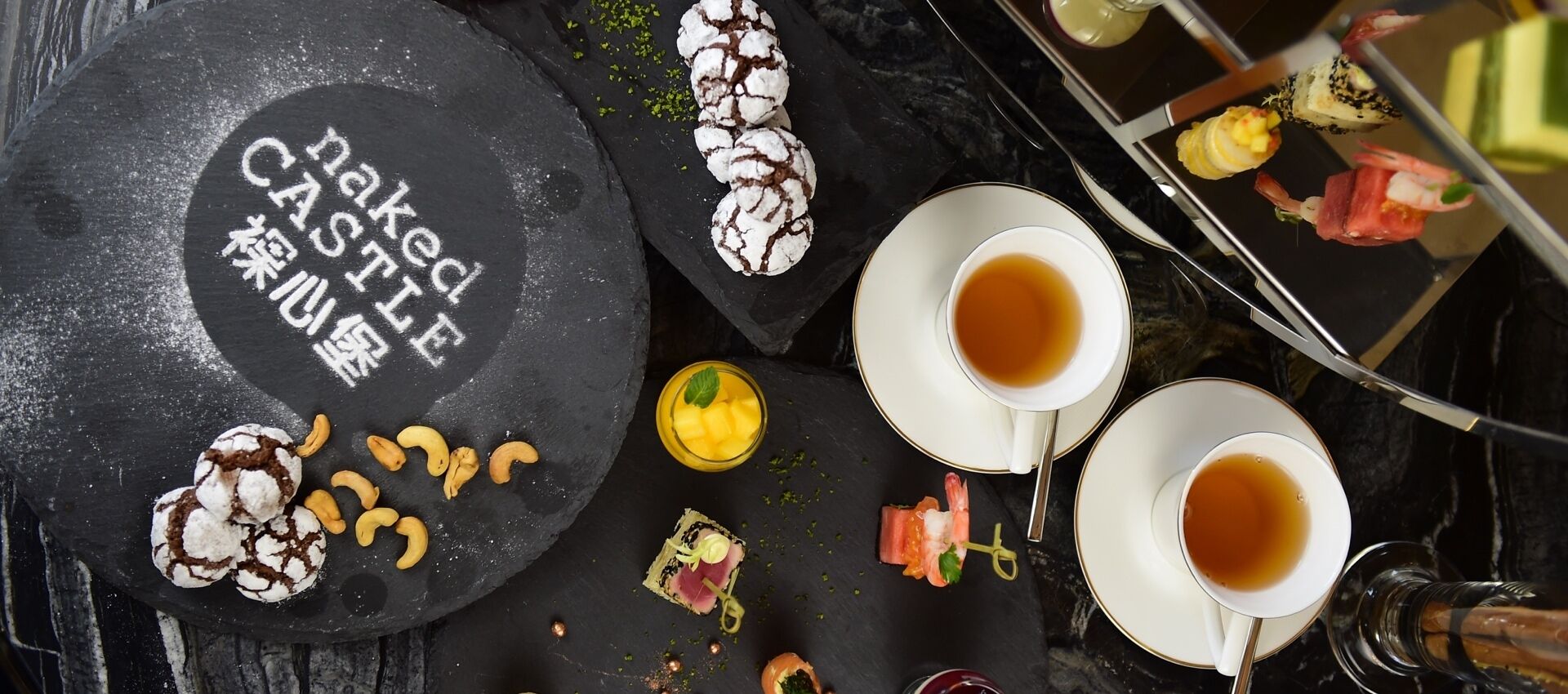 A slate serving board with food items and two cups of tea.