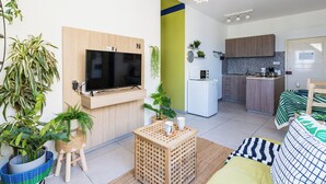 A modern apartment with a flat-screen TV, a kitchen with a microwave, and a dining area with a green-striped tablecloth. - Whispering Palms 1-BR Apt. By Finikoudes Beach (Larnaca)